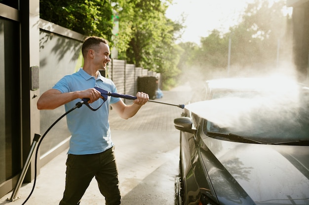 Homem possui pistola de água de alta pressão, estação de lavagem automática. Indústria ou negócio de lavagem de carros. Indivíduo do sexo masculino limpa seu veículo de sujeira ao ar livre
