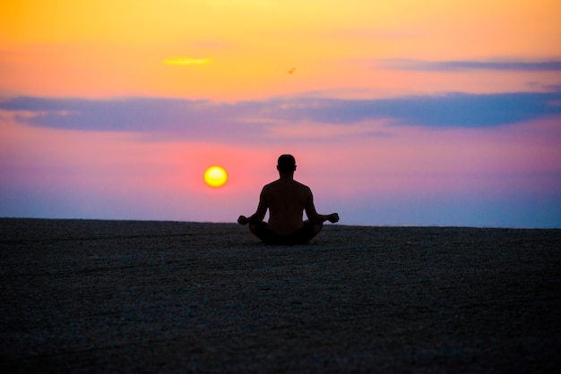 Homem pratica ioga na praia, o mar pela manhã, ao nascer do sol.