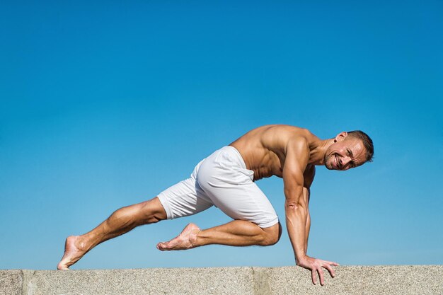 Homem praticando ioga fundo de céu azul. Alcançou paz de espírito. Conceito de meditação e ioga. A ioga ajuda a encontrar o equilíbrio. Pratique asana ao ar livre. A prática de ioga ajuda a encontrar harmonia e equilíbrio.