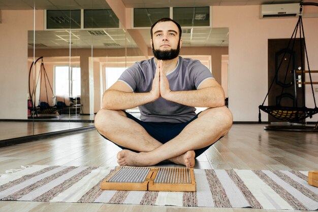 Homem praticando ioga, meditando, sentado com as mãos unidas no chão perto de uma placa de sadhu