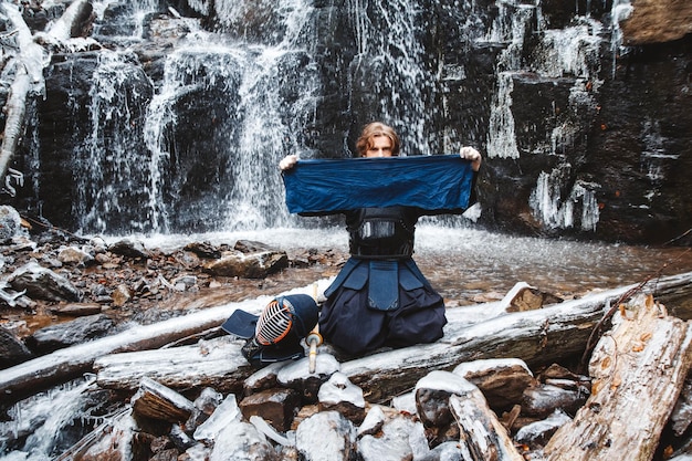 Homem praticando kendo com espada de bambu no fundo da cachoeira