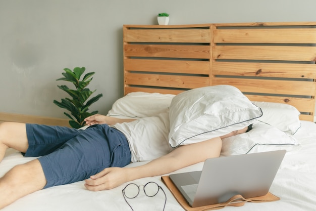 Homem preguiçoso com sono está trabalhando em casa, mas dorme na frente do laptop.