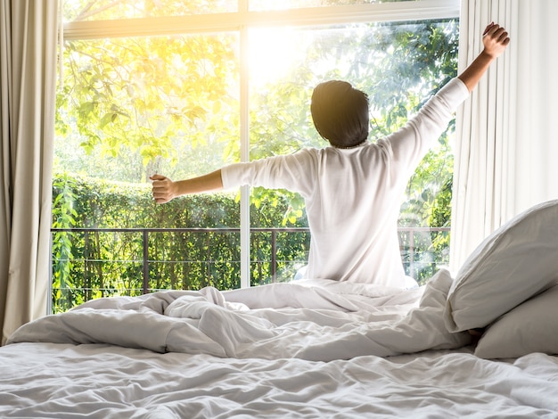 Homem preguiçoso feliz acordar na cama levantando as mãos de manhã com sentimento fresco