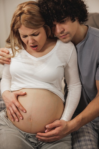 Foto homem preocupado consolando sua esposa grávida em um quarto que está tendo contrações pré-natais.