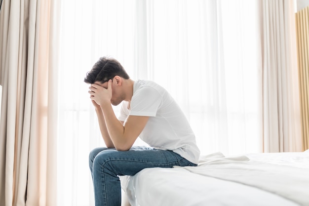 Homem preocupado ou deprimido, sentado na cama com a mão na testa