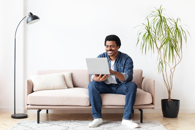 Homem preto sentado no sofá usando um computador portátil