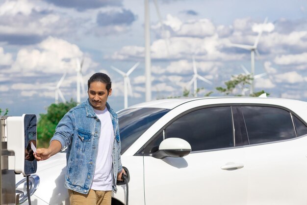 Homem progressivo com seu carro EV e turbina eólica como conceito de energia renovável