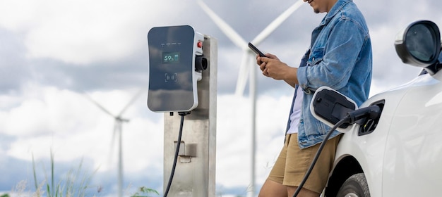 Homem progressivo com seu carro EV e turbina eólica como conceito de energia renovável