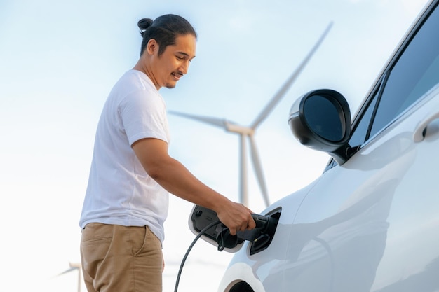 Homem progressivo com seu carro EV e turbina eólica como conceito de energia renovável