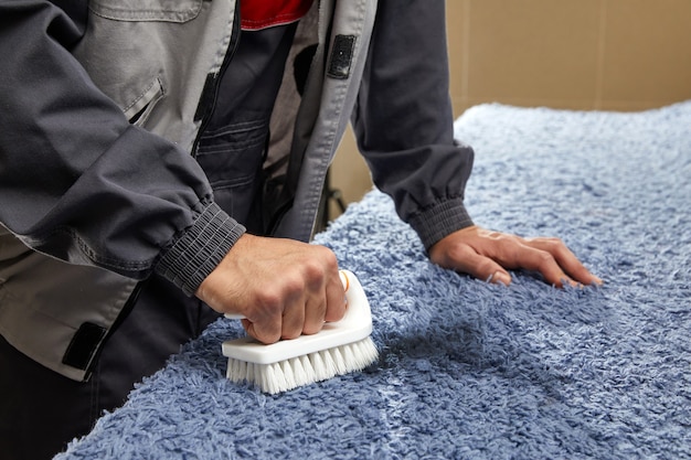 Foto homem pulverizando detergente no carpete cinza para remover manchas em serviço de limpeza profissional