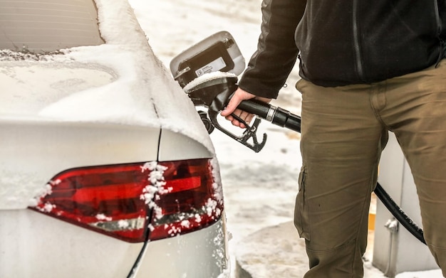 Homem que enche o tanque de gás do carro diesel coberto de neve na bomba de combustível, detalhe disponível e bocal de gasolina.