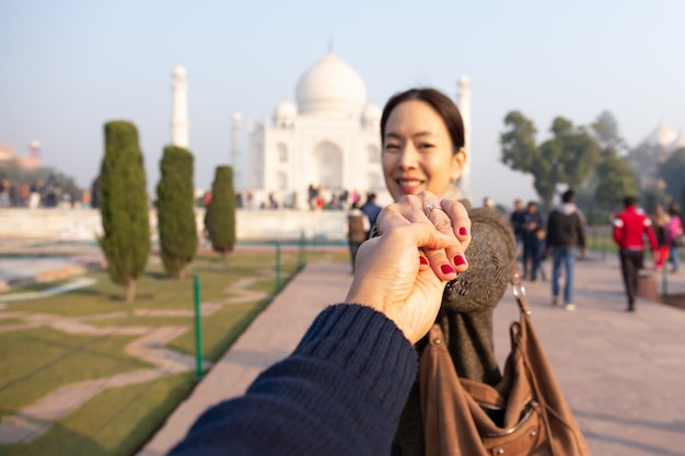 Foto homem que guarda sua mão da esposa que mostra a aliança de casamento com taj mahal no fundo.