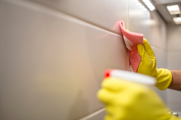 Homem que limpa móveis de cozinha por roupa amarela