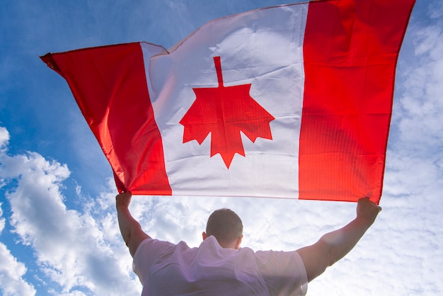 Foto homem que mantém a bandeira nacional do canadá contra o céu azul