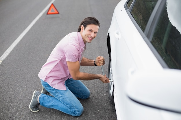 Foto homem que muda a roda após uma queda no carro