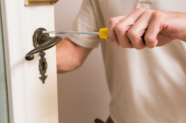 Homem que repara o punho da porta com uma chave de fenda