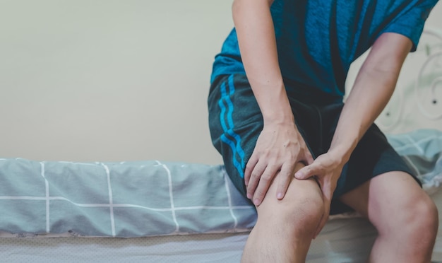 Homem que sofre de dor no joelho sentado na cama problema de saúde e conceito de pessoas