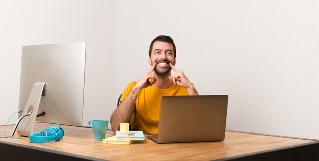 Homem que trabalha com laptot em um escritório, sorrindo com uma expressão feliz e agradável