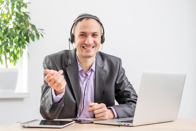 Homem que trabalha no escritório do amanhecer ao anoitecer. Comunicação através da Internet. Jovem empresário usando tablet laptop e fones de ouvido conectando wi-fi. Luz do pôr do sol. Negociações online.