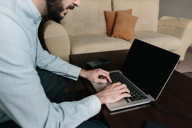 Homem que trabalha on-line com um laptop sentado no sofá em casa. teletrabalho e conceito de trabalho remoto