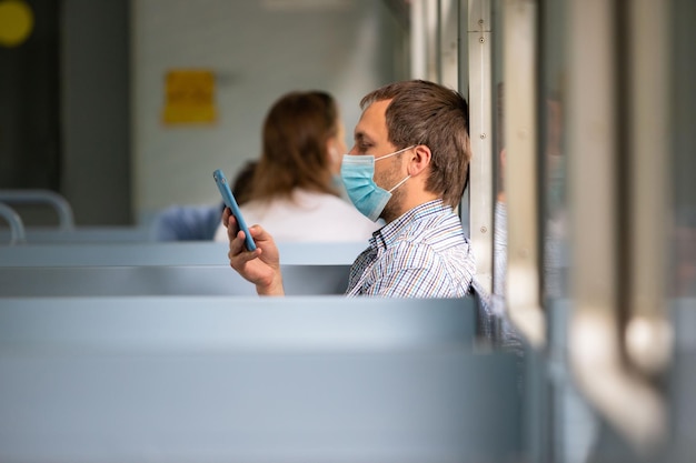 Foto homem que usa smartphone usa máscara de proteção no trem para proteger o sistema respiratório de infecção