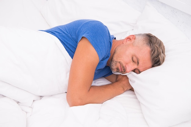 Homem relaxado. Promova a prevenção e o controle dos distúrbios do sono. Dia Mundial do Sono. Benefícios de um sono bom e saudável. Respire facilmente, durma bem. Homem bonito na cama. Cara dormindo em casa.