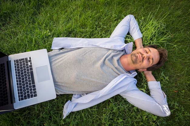 Homem relaxando na grama no verão, com laptop na barriga