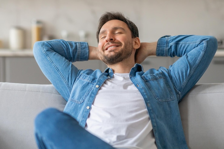 Foto homem relaxando no sofá com os olhos fechados e as mãos atrás da cabeça