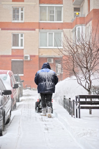 Homem remove a neve no quintal de um edifício de vários andares com máquinas de neve