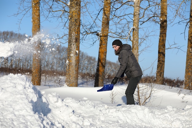 Homem remove neve com uma pá da estrada em um dia de inverno