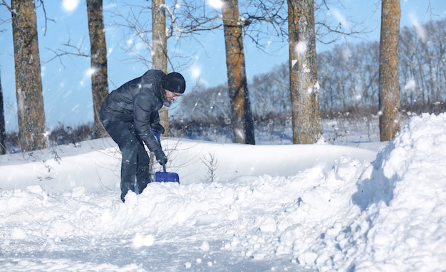 Homem remove neve com uma pá da estrada no inverno nevado