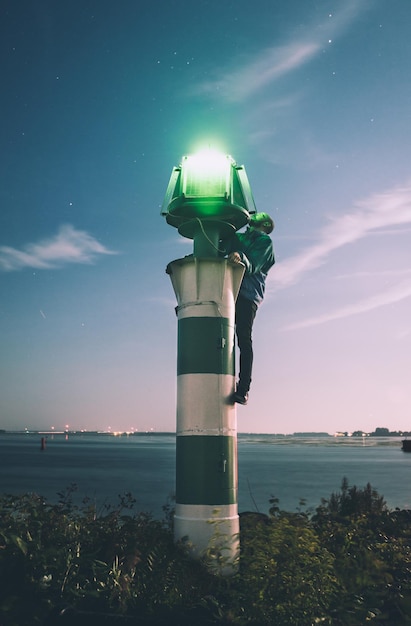 Homem reparando farol contra o céu ao anoitecer