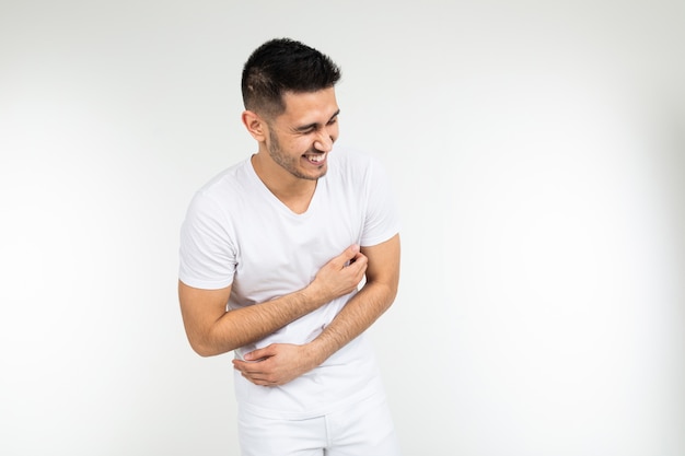 Homem rindo e segurando a barriga em um fundo branco do estúdio, com espaço de cópia.