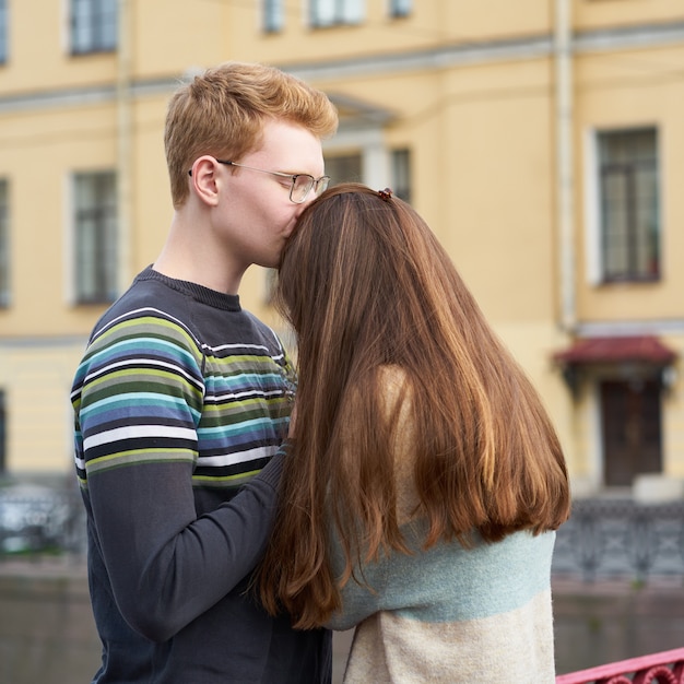 Homem ruivo beija uma mulher no topo da cabeça, um garoto de suéter acalma