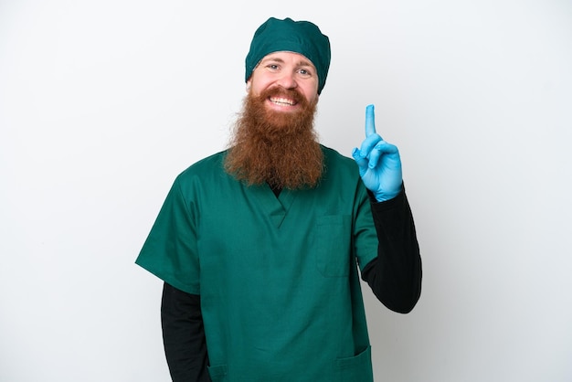 Homem ruivo cirurgião de uniforme verde isolado em fundo branco mostrando e levantando um dedo em sinal do melhor