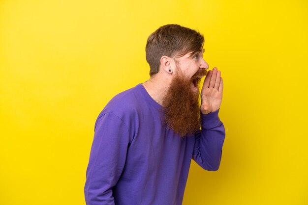 Homem ruivo com barba isolada em fundo amarelo gritando com a boca aberta para o lado