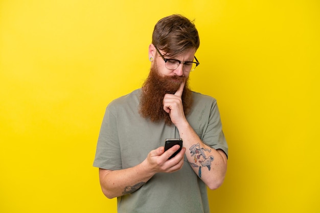 Homem ruivo com barba isolada em fundo amarelo pensando e enviando uma mensagem