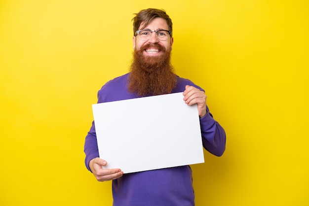 Homem ruivo com barba isolada em fundo amarelo segurando um cartaz vazio com expressão feliz