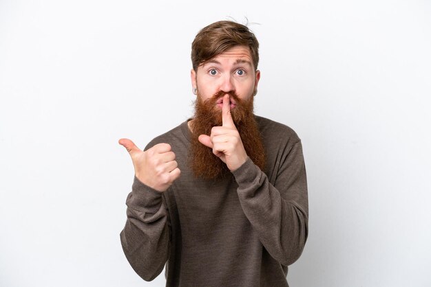 Homem ruivo com barba isolada no fundo branco, apontando para o lado e fazendo o gesto de silêncio