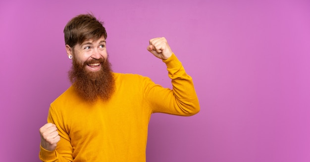 Homem ruivo com barba longa ao longo da parede roxa comemorando uma vitória