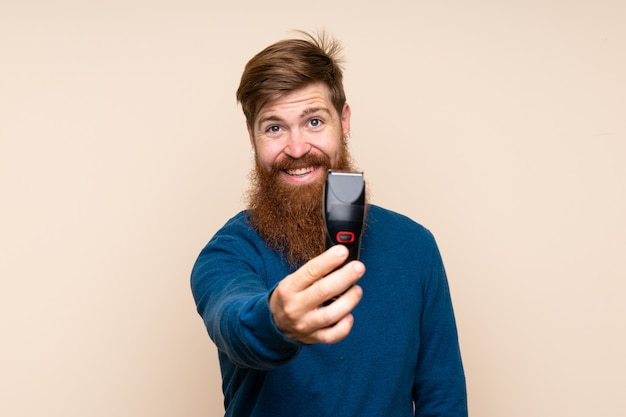 Homem ruivo com barba longa com vestido de cabeleireiro ou barbeiro e segurando a máquina de corte de cabelo