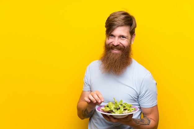 Homem ruivo com barba longa e com salada ao longo da parede amarela