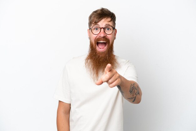 Homem ruivo com barba longa isolado no fundo branco surpreso e apontando para a frente