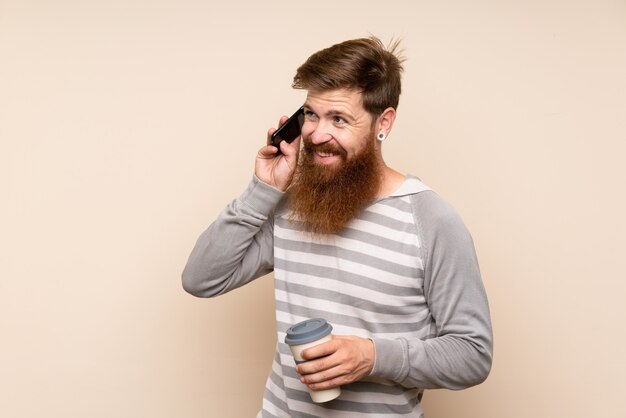 Homem ruivo com barba longa segurando café para tirar e um celular