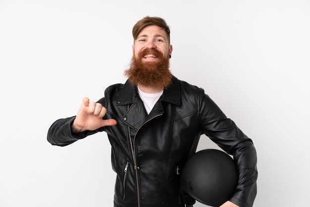 Foto homem ruivo com barba longa, segurando um capacete de motocicleta sobre parede branca isolada, orgulhoso e satisfeito