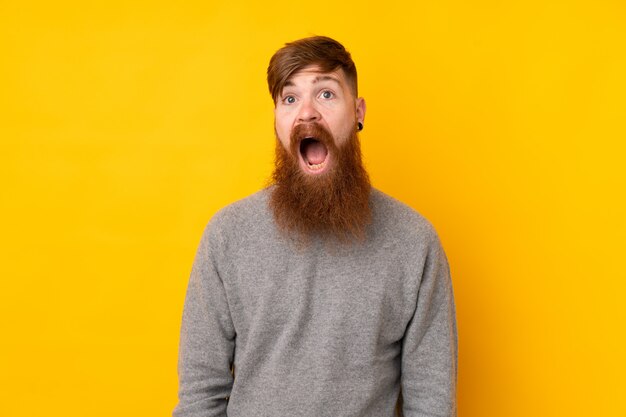 Homem ruivo com barba longa sobre parede amarela isolada com expressão facial de surpresa