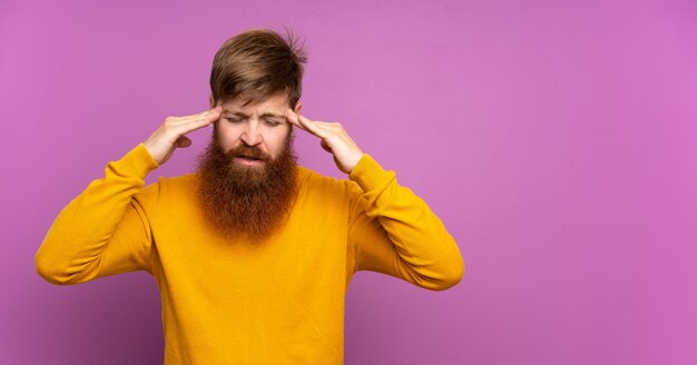 Homem ruivo com barba longa sobre roxo isolado com dor de cabeça