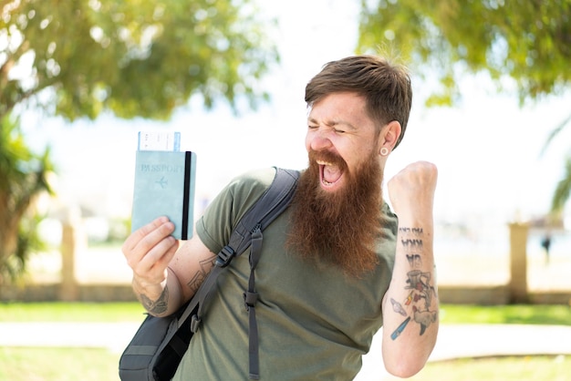 Homem ruivo com barba segurando um passaporte ao ar livre comemorando uma vitória