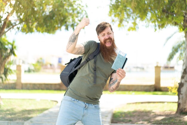 Homem ruivo com barba segurando um passaporte ao ar livre comemorando uma vitória