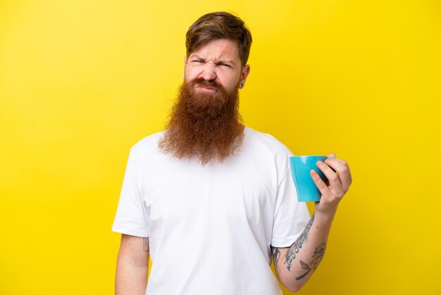 Homem ruivo com barba segurando uma caneca isolada em fundo amarelo com expressão triste